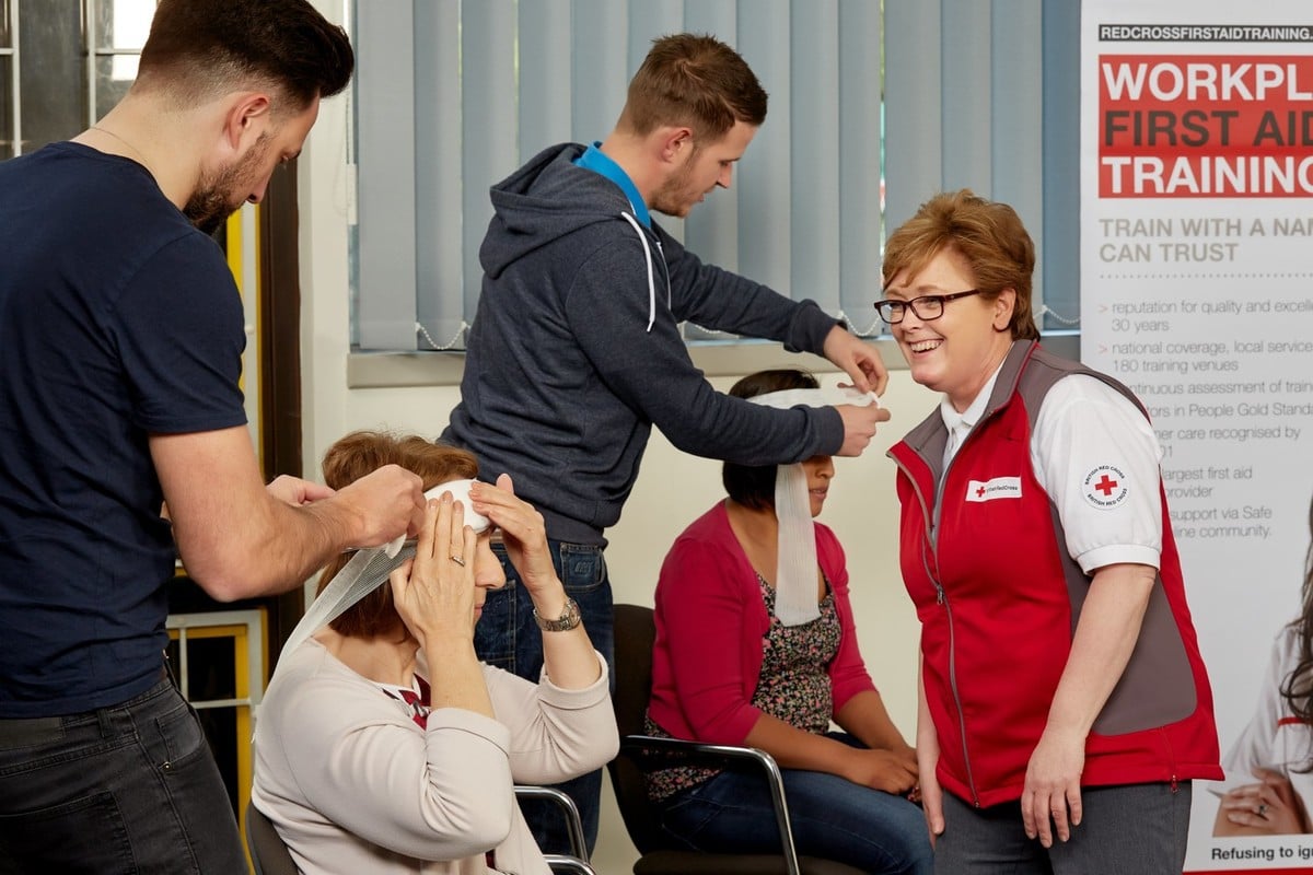 A group of First Aid at Work course attendees, learning how to properly put a bandage on someones head by a British Red Cross trainer. 